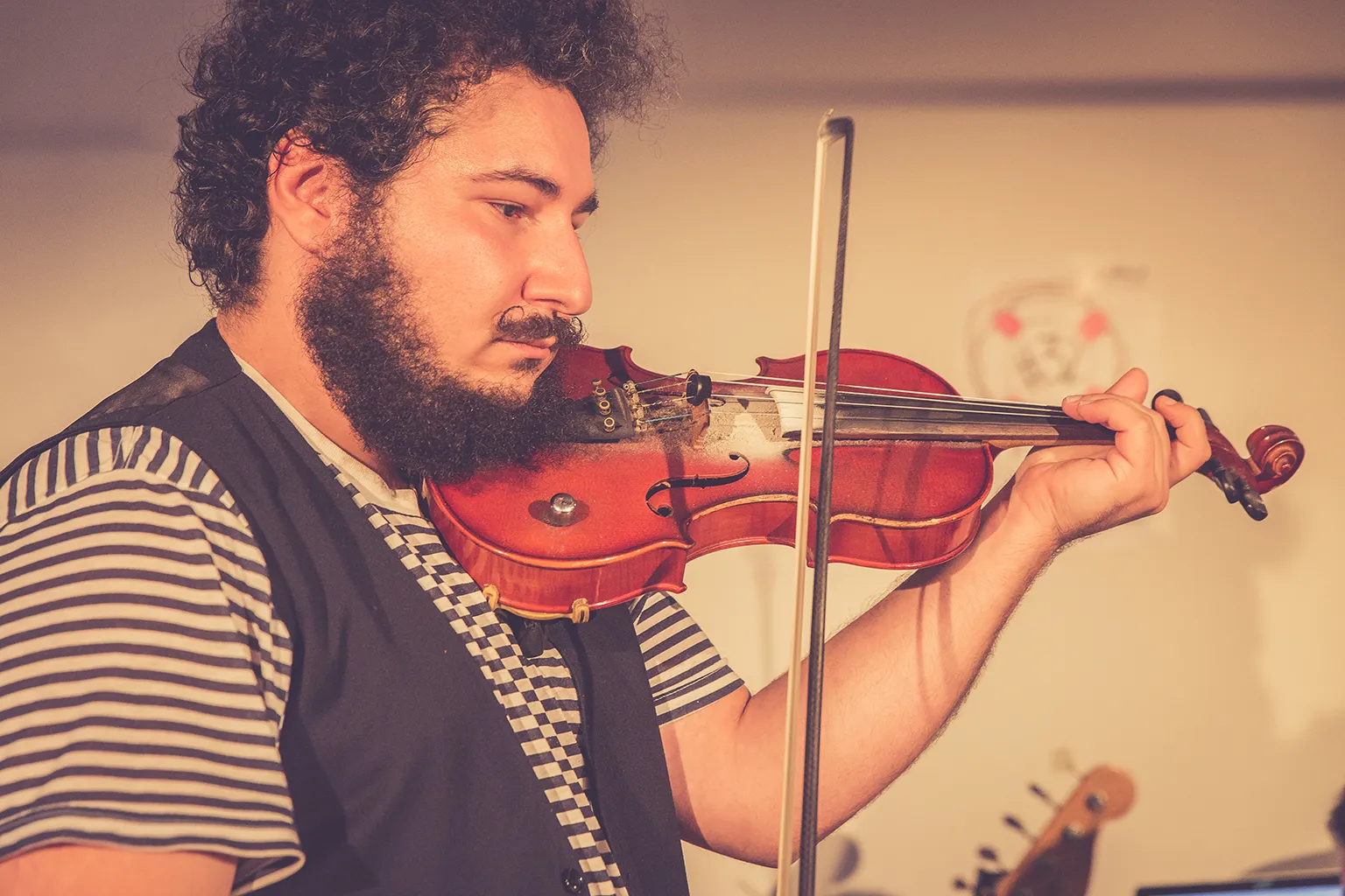 Alex Burkoy playing violin on stage, eyes lowered in concentration, bow held upright
