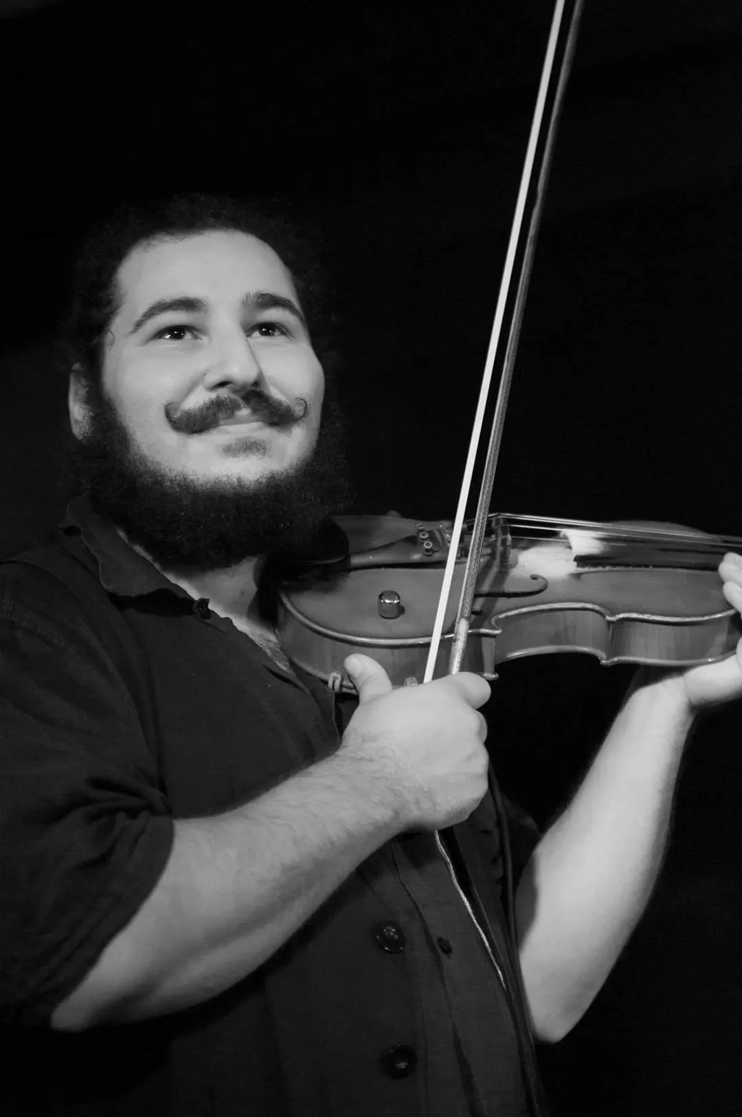 Black and white portrait of a smiling bearded violinist with a waxed moustache, bow raised
